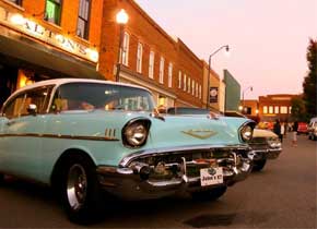 A light blue classic car parked in front of a red brick building