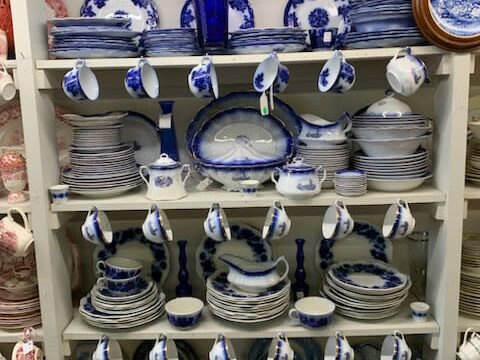 White shelves display white and blue plates, teacups, teapots, and serving dishes