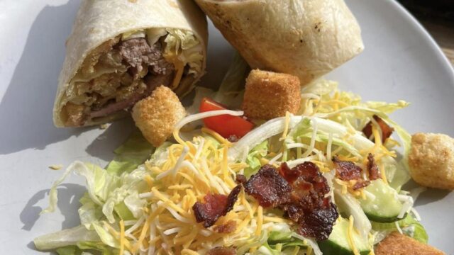 A round white plate with a burrito sliced in half and a salad