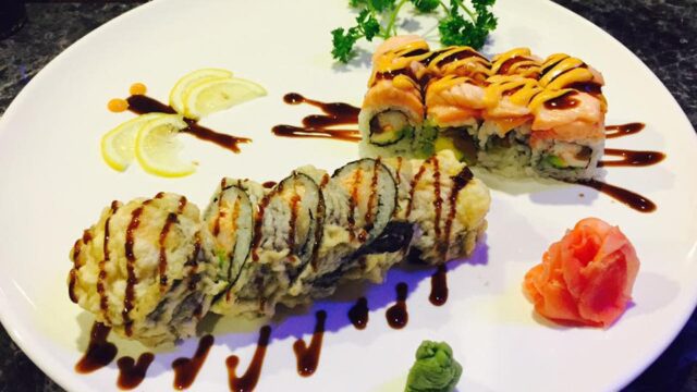 Two sushi rolls, wasabi and ginger displayed on an oval white plate